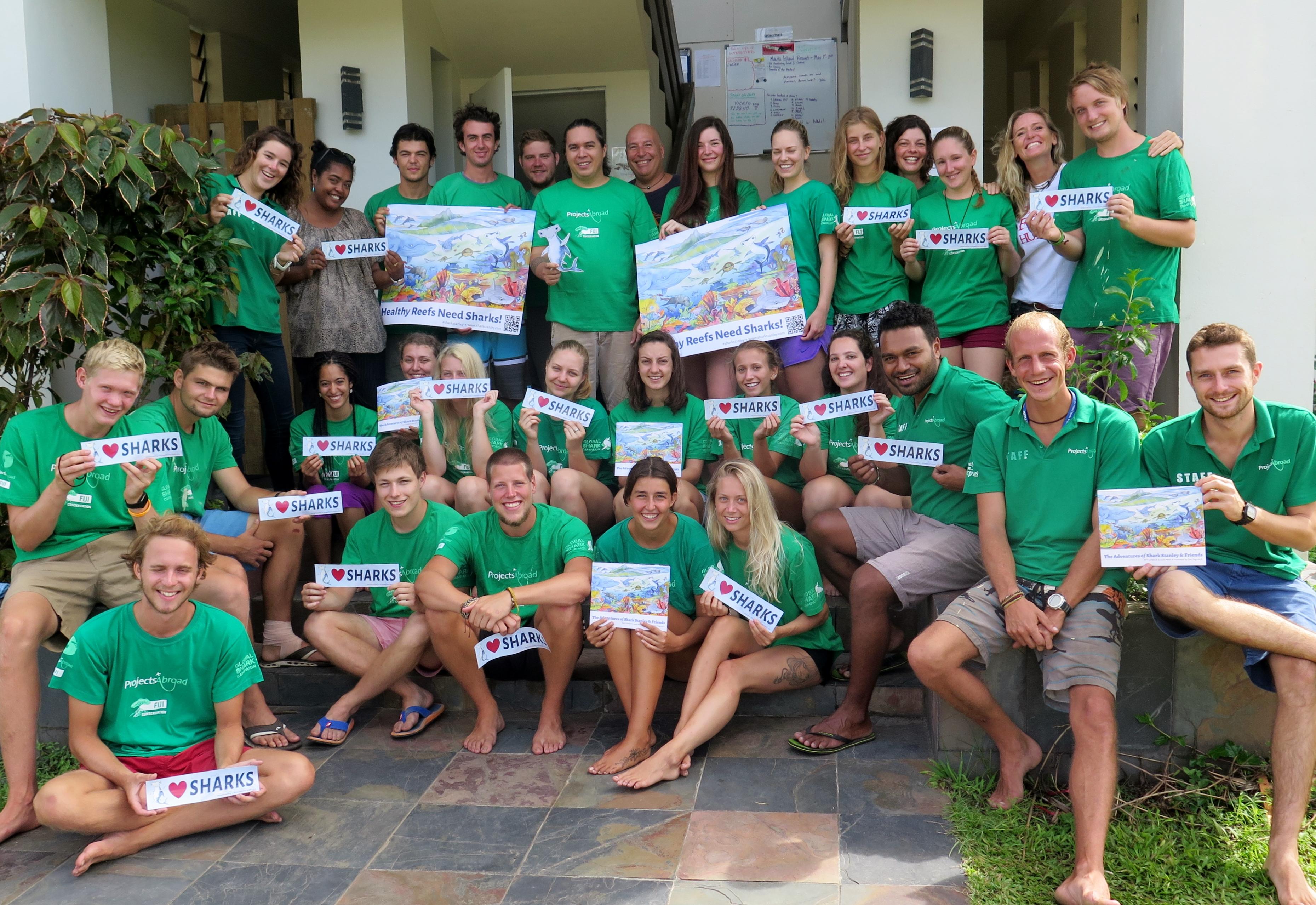Un grupo de estudiantes informando sobre la importancia de conservar a los tiburones en su voluntariado ambiental en Fiyi. Jóvenes voluntarios creando consciencia sobre la conservación de tiburones en Fiyi.